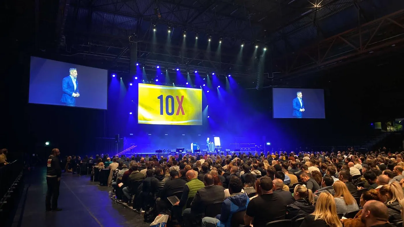 Grant Cardone on stage at a 10X arena event, with IMAG side screens and a packed audience